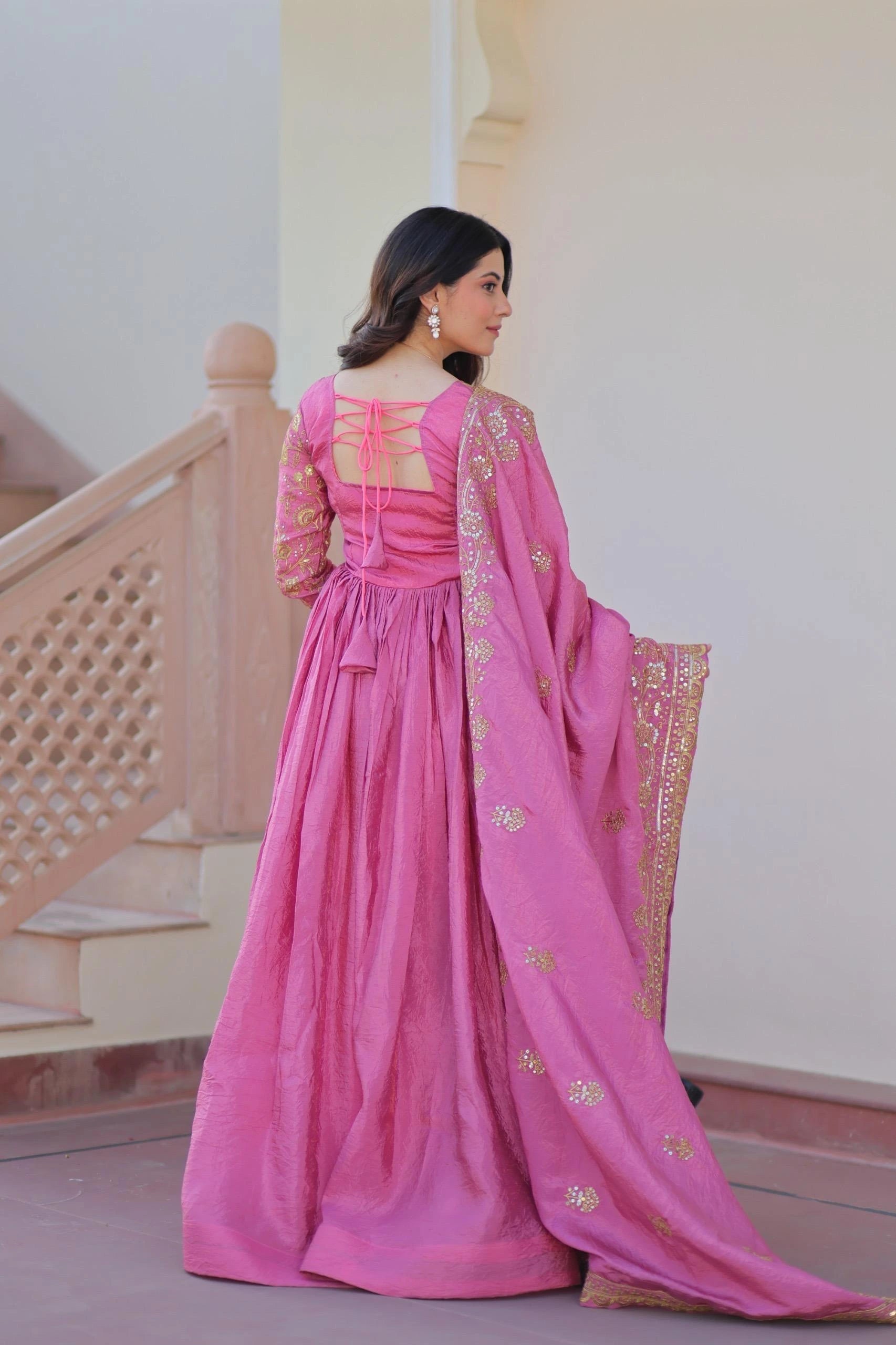 Woman in a pink traditional outfit with gold embroidery sitting on a bench.